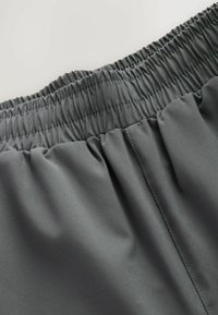 Tela gris con una cintura elástica fruncida, que muestra una textura suave y un brillo sutil. Detalle de costura visible en el lateral.