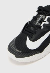 Musta urheilujalkine, jossa on teksturoitu yläosa, vahva valkoinen Nike-logomerkki ja uurrettu kumipohja. Nyörit ja verkkokangas ovat mukana.