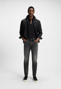 Giacca nera, polo nera con colletto beige, jeans grigi e sneakers nere. Tessuto morbido, vestibilità su misura e accenti minimi.