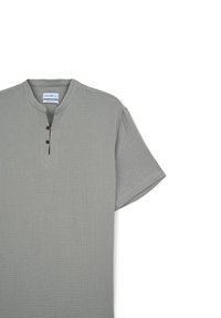 Maglietta grigia a maniche corte realizzata in tessuto testurizzato, con scollatura rotonda, chiusura a tre bottoni e una vestibilità morbida.