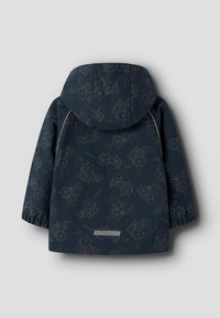 Veste imperméable bleu marine avec un motif de tracteur, capuche, poignets élastiques et une bande réfléchissante à l'ourlet. Texture lisse, matériau léger.