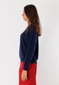 Maglione a maglia blu navy con maniche lunghe e una vestibilità rilassata. Presenta un collo a giro e orlo a costine. Abbinato a pantaloni rossi.
