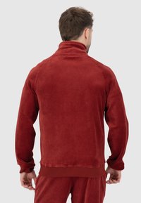 Rote Fleecejacke mit hohem Kragen, gerippten Bündchen und Saum. Weiche Textur, taillierte Silhouette, saubere Nähte und glatte Stoffoberfläche.