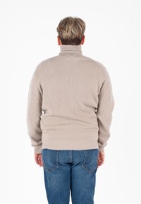Beige geribbelde coltrui met lange mouwen, voorzien van een getailleerde taille en een zachte textuur, gecombineerd met blauwe spijkerbroeken.