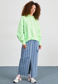 Mintgrön oversized hoodie, blårandig cargokjol med framklippningar och vita sneakers med röda accenter. Släta ytor och en avslappnad design.