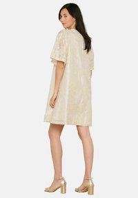 Kerge beež kleit lillelise tekstuuriga, lühikesed varrukad ja lõdva lõikega, millele on sobitatud läikivad kuldsed plokkninaga sandaalid.