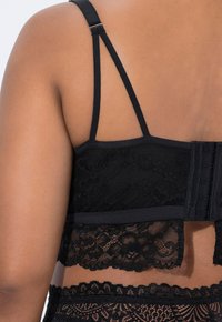 Černá krajková podprsenka s nastavitelnými ramínky, s texturovaným krajkovým páskem a zapínáním na háček a očko. V designu jsou složité květinové vzory.