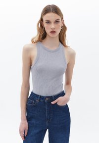 Šedý žebrovaný top na ramínka s kulatým výstřihem, v kombinaci s tmavě modrými džínami s vysokým pasem, které mají knoflík a kapsy. Celkově hladká textura.