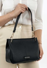 Borsa a tracolla in pelle nera con superficie testurizzata, due dettagli in metallo dorato e una sola tracolla. Presenta un discreto logo applicato.