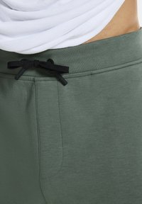 Groene katoenen sweatpants met een zwarte trekkoord, met een gladde textuur en een zijzak. De tailleband is elastisch voor extra comfort.