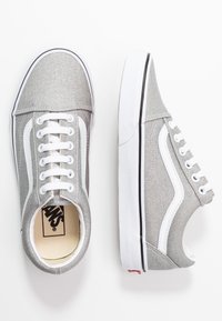 Šedé plátěné tenisky s bílými akcenty, ploché bílé tkaničky a gumová podrážka s černým pruhem podél okraje. Uvnitř logo Vans.