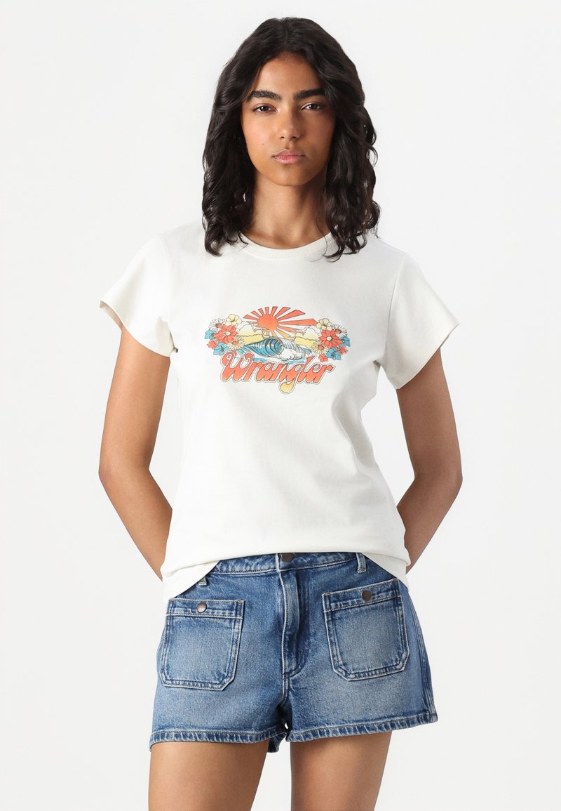 Kremowa koszulka z bawełny z krótkim rękawem i okrągłym dekoltem, z kolorową grafiką kwiatów i słońca oraz napisem "Wrangler". W komplecie z niebieskimi szortami dżinsowymi.