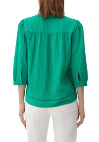 Grüne, strukturierte Bluse mit Dreiviertelärmeln, offenen Seitenschlitzen und abgerundetem Saum. Verfügt über eine geraffte Passe und Knopfdetails.