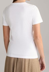 Camiseta blanca de algodón con mangas cortas, escote redondo, textura suave y un diseño simple y sin adornos, combinada con una falda beige.