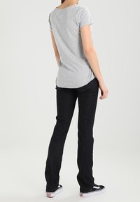 Camiseta ajustada gris de manga corta, combinada con jeans azul oscuro y zapatillas Vans negras con suelas blancas, vista desde la espalda.