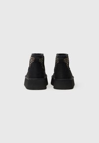 Sapatos altos em camurça preta com detalhes de tachas no calcanhar, acabamento texturizado e uma sola espessa de borracha preta.