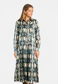 Vestido de manga larga y botones con tejido estampado que presenta formas geométricas en tonos verde azulado, verde, marrón y crema; con cintura ajustada.