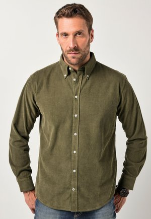 Chemise en velours côtelé vert olive avec un col à boutons, des manches longues et une texture côtelée visible ; elle présente des boutons blancs et un ourlet arrondi.