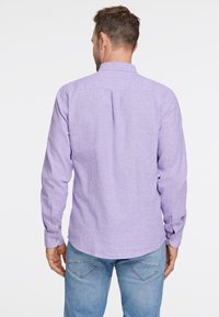 Camisa de manga larga morada clara con cuello, yugo trasero y puños abotonados, hecha de una tela texturizada. Usada con vaqueros azules.