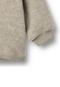 Manica di maglione beige in lana con polsino e orlo a coste visibili, che mostrano una morbida texture e dettagli di maglieria accogliente.