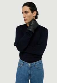 Gants en cuir noir, pull bleu marine et jean bleu clair. Le pull a des manches longues ; les gants présentent des coutures et un design ajusté.