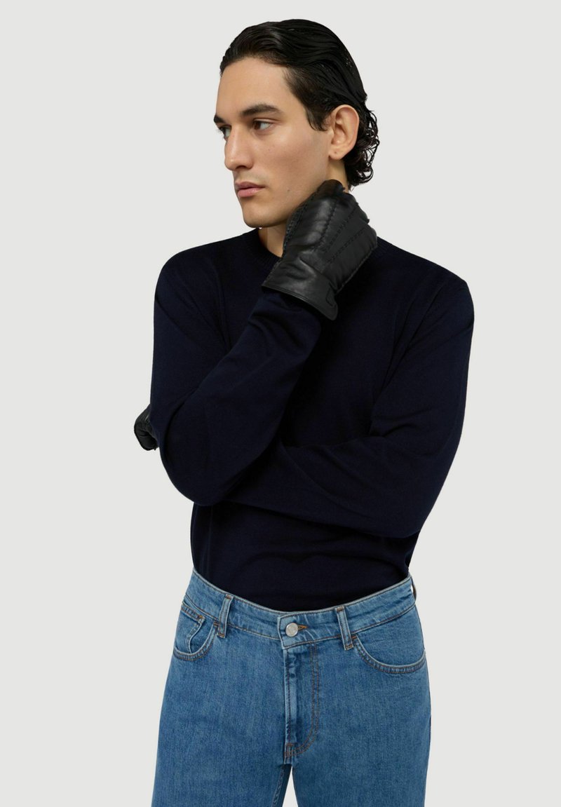 Gants en cuir noir, pull bleu marine et jean bleu clair. Le pull a des manches longues ; les gants présentent des coutures et un design ajusté.