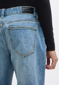 Φωτεινό γαλάζιο τζιν παντελόνι με μέση μέτριου ύψους, που διαθέτει πίσω τσέπη με αντίθετη πορτοκαλί ραφή και μαύρη δερμάτινη ετικέτα στο πίσω μέρος.