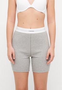 Calções de jersey cinzentos canelados com uma cintura elástica branca que apresenta a marca Calvin Klein. O tecido é suave com um design ajustado.