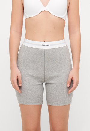 Sive rebraste trenirke s bijelim elastičnim pojasom na kojem je brend Calvin Klein. Tkanina je meka i ima uski kroj.