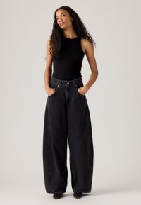 Czarne dżinsy o szerokich nogawkach w połączeniu z czarnym topem bez rękawów. Spodnie mają wysoki stan i przednie kieszenie, a ich krój jest luźny.