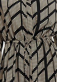 Robe noire ornée d'un motif de grands pois blancs disposés en chevrons, avec une taille froncée et une texture de tissu lisse.