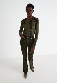 Maglione lungo a maniche con coste in verde oliva, decorato con un motivo tie-dye, abbinato a pantaloni in corduroy verde scuro; modella che indossa scarpe metalliche a punta.