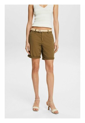 Kvinde iført olivengrønne shorts med opbukket kant, beige flettet bælte, hvid ærmeløs strik top og beige højhælede sandaler.