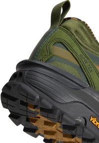 Gros plan sur le talon d'une chaussure de randonnée verte et noire avec une semelle en caoutchouc texturée et une tige en tissu Gore-Tex avec languette pour une utilisation en extérieur.