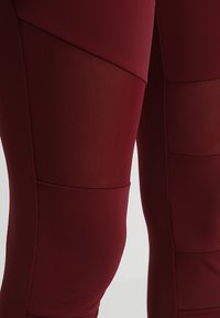 Burgundi leggings, sima és texturált panelek keverékével, geometrikus formákkal és kényelmes, testhez álló kialakítással.