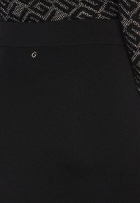 Tissu noir côtelé avec une texture lisse, présentant un motif décoratif en haut et un petit logo métallique près de la taille.