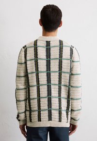 Strickjacke in Beige mit einem strukturierten Muster. Verfügt über ein kariertes Design in dunklem Grün, Marineblau und gelben Akzenten. Rippbündchen und Saum.