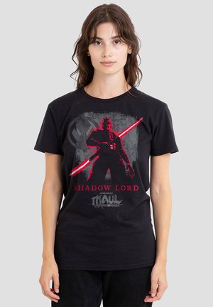 Junge Frau trägt ein schwarzes T-Shirt mit rotem und grauem Grafikbild des Star Wars-Charakters Maul, der ein doppelklingiges rotes Lichtschwert hält.