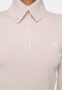 Jasnoróżowa koszulka polo z rypsowym kołnierzykiem, pięcioma guzikami i białym logo na piersi. Miękka, dopasowana dzianina.