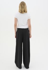 Wide-leg black trousers with a smooth texture, featuring two back pockets and a tailored waistband. Worn with a plain white t-shirt.