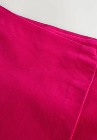 Helles pinkfarbenes Cordstoff mit gerippter Textur, ordentlich gefaltet. Die Farbe ist kräftig, und die Oberfläche zeigt feine vertikale Rillen.