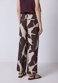 Brede beenbroek in een bruine en crèmekleurige abstracte print. Gemaakt van lichte stof met een textuur gevoel. Voorzien van een elastische tailleband.