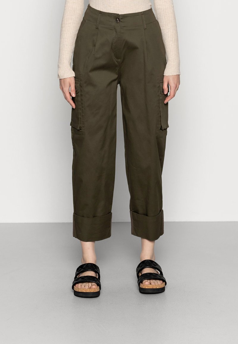 Pantaloni cargo di colore verde oliva, con vita alta, tasche laterali e orli risvoltati. Abbinati a sandali neri a più cinghie.