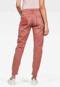 Vaqueros de mezclilla rosa con forma ajustada, diseño de cinco bolsillos y detalles de costura sutil. Llevados con zapatillas blancas, mostrando un look casual.