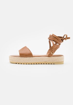 Brune læder espadrille sandal med flad platform, åben tå og flettet stropdesign. Anklerne omsluttet med bindelukning. Jute mellemsål.