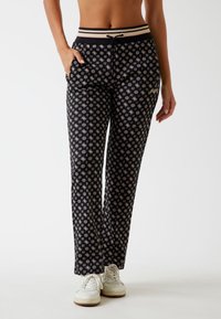 Pantaloni neri con un motivo floreale bianco, vita elastica con cordino e tasche laterali. Abbinati a sneakers bianche.