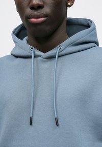 Hættetrøje i lyseblåt bomuldsstof med en glat tekstur, der har matchende snore og metalspidser.