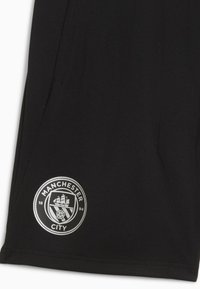 Shorts de sport noirs avec le logo de Manchester City, qui comprend un navire et le texte "Manchester City" autour d'un design circulaire.
