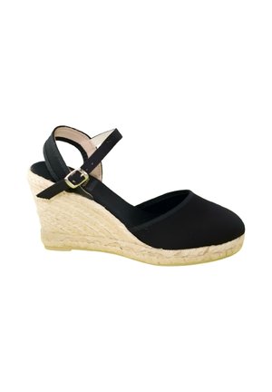 Alpargata negra con puntera cerrada, cuña de yute trenzado, correa en el tobillo y hebilla plateada sobre fondo blanco.