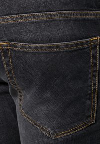 Tmavě modré džíny z denimu s zadní kapsou zdobenou žlutým prošitím. Látka má jemnou texturu a hladký povrch.